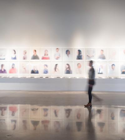 blurred person walking by installation of photographs on wall of gallery
