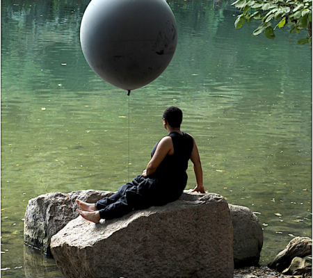 Still from film from Ariel Rene Jackson depicting Black woman with black balloon sitting beside body of water