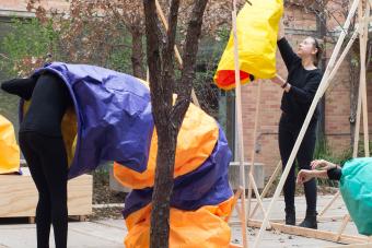 students in performance piece involving colored paper sleeves and wooden structure