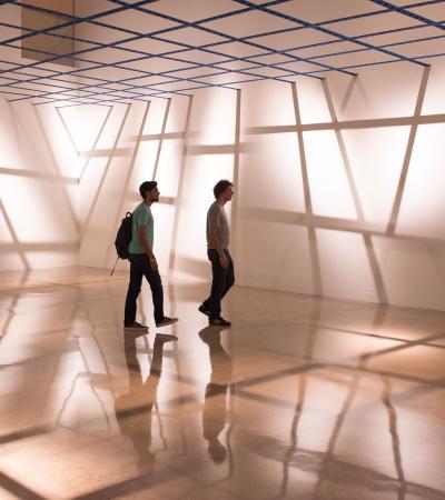 people in gallery with linear shadows cast on floor and walls by tape