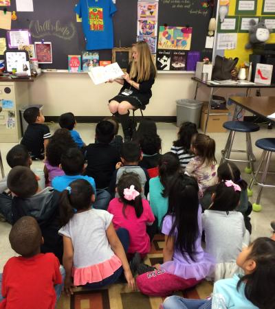 student teaching reading book aloud to group of elementary students