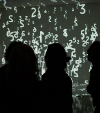three figures in silhouette against a projection of numbers