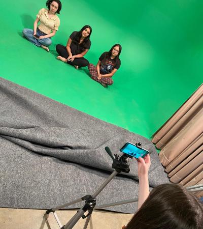 students sitting in front of green screen with camera on tripod in foreground