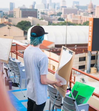 student drawing at easel overlooking UT football stadium