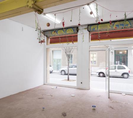 image of an open air gallery with clay covering its floor and flowers and coke cans strung up on lines on the ceiling