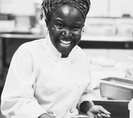 black and white portrait of smiling Black woman in chef's coat 
