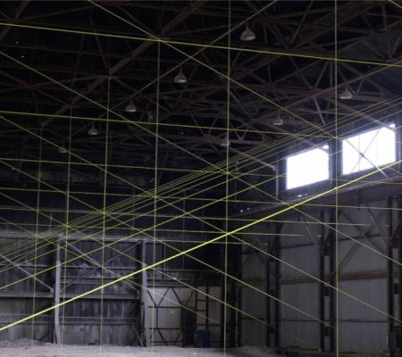 The inside of a large grey warehouse with two windows and neon yellow rope creating lines all over