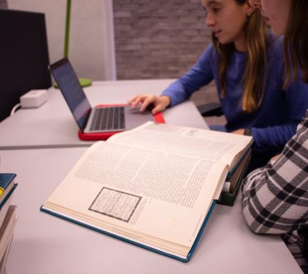 two women in library consulting a book in front of a laptop