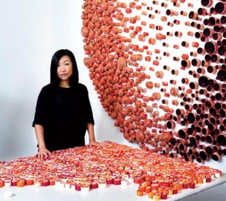 UT Austin Professor Beili Liu in front of an installation of her work to her right and a display of her materials on a table in front of her