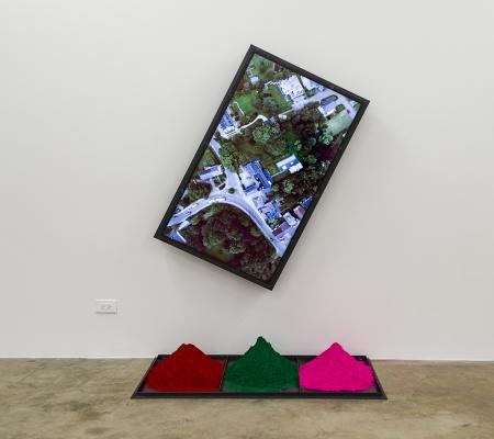 installation view of aerial photo on screen and three piles of red green and pink dye