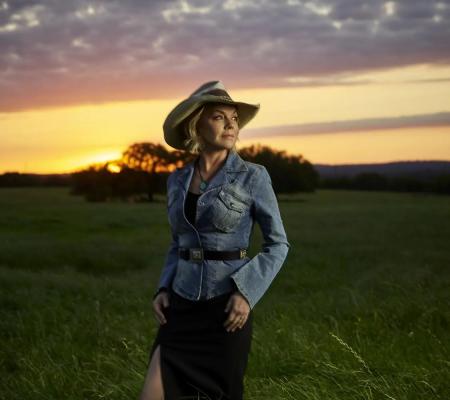 woman wearing hat standing in a field in front of a sunset