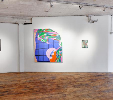 an open gallery space with white walls and brown wooden floors. there are paintings hanging on the walls, each in different styles and multiple, bright colors