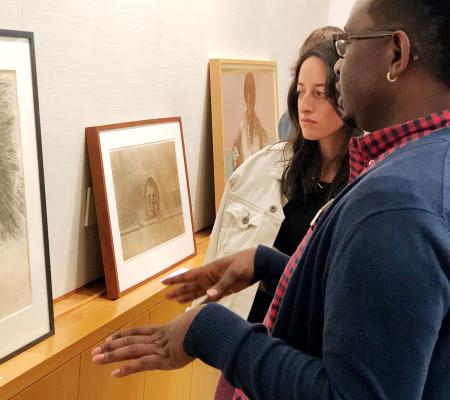 two people looking at and discussing framed prints on shelf 