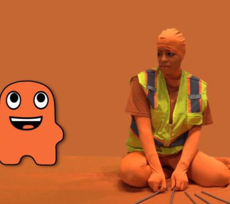 orange character sits opposite artist dressed in orange bodysuit against an orange backdrop