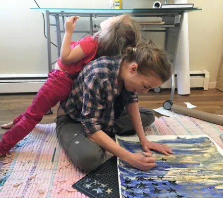 image of woman drawing with child leaning against her back