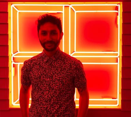 image of tomas rivera standing in front of a neon artwork