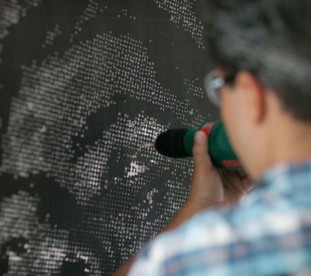 Image of UT Austin alumnus in Printmaking Miguel Aragon at work on large scale piece burning out holes in a print and seen from behind