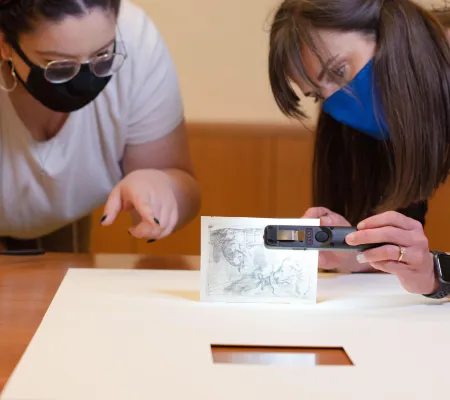 UT Austin undergraduate Art History major Natalie Ponder looking at print archive collection piece with curator Holly Borham