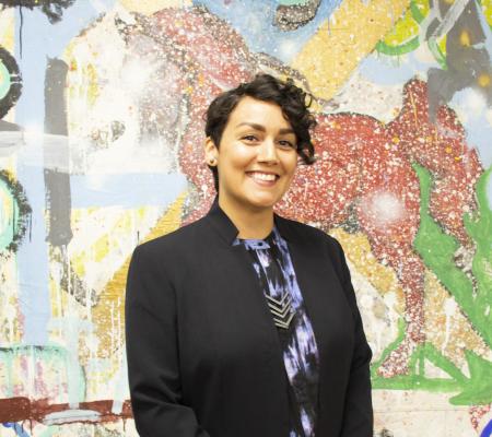 image of woman in black blazer in front of latino artist mural