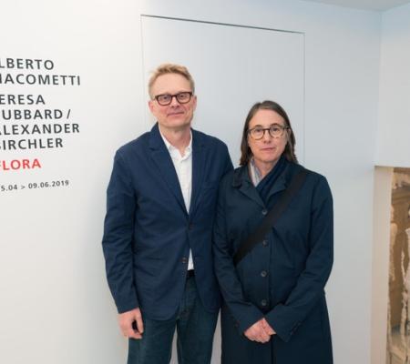two artists standing in front of title text for exhibition on wall behind them
