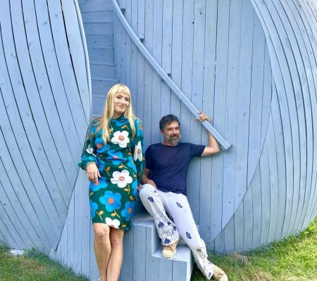 Two people sit on stairway within a blue wooden sculpture.