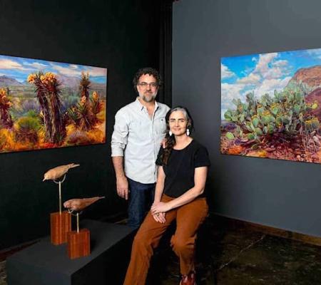 Two artists sitting in front of paintings on the wall