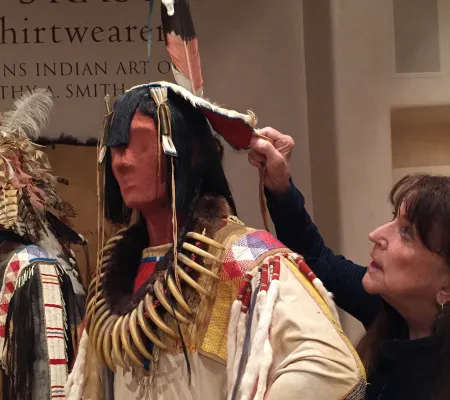 a brunette woman lifting up headdress on native mannequin 
