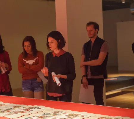 white brunette woman looks down in front of waist height exhibition display in the Visual Arts Center while educating students behind her