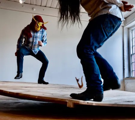 Two masked figures performing on circular wooden platform in St. Elmo artist fellow at The Universit