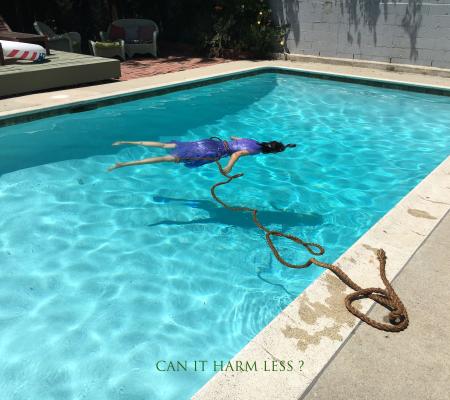 woman in purple dress floating in pool face down with rope spooling from waist to poolside