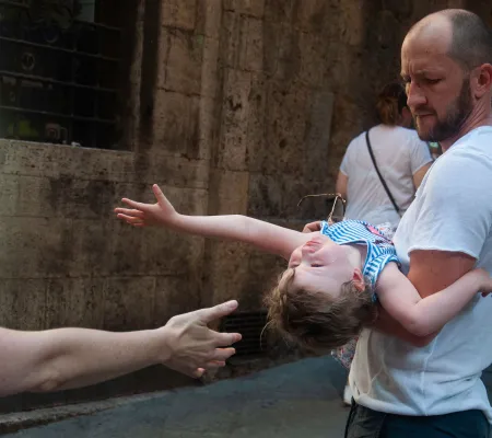 small child leaning back in a man's arms to reach another hand coming in from outside the frame