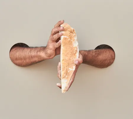 two arms inserted through two holes cut into a taupe wall holding a stone vertically in a piece from artist Shadi Harouni who will be visiting UT Austin Department of Art and Art History for its Visiting Artist Lecture Series 