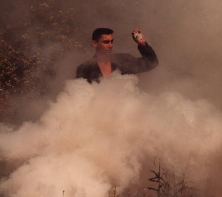 brown tinted photograph of man standing behind brush and smoke