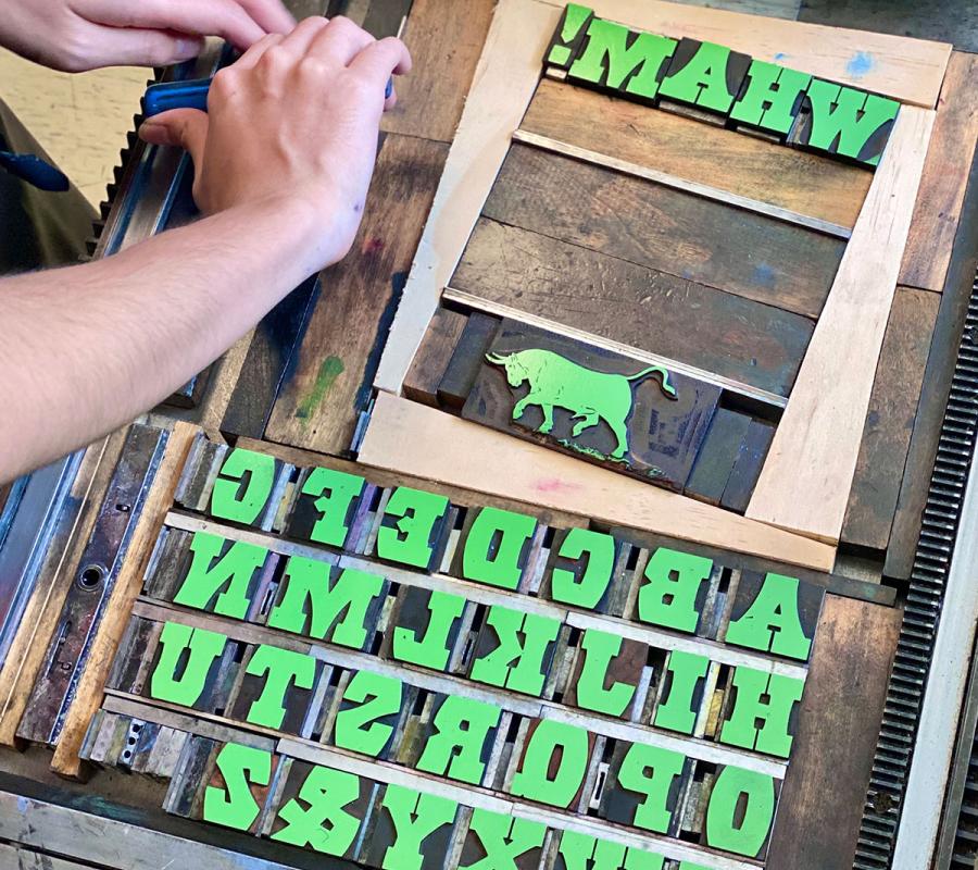 person locking up wooden type on bed of printing press