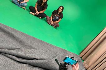 students sitting in front of green screen with camera on tripod in foreground