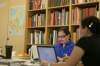 two people working on laptops in room with wall of books