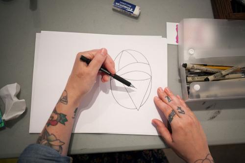 overhead view of hands drawing on a sheet of paper