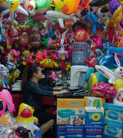 woman sitting in market stall crammed with inflatable toys