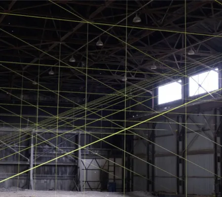 The inside of a large grey warehouse with two windows and neon yellow rope creating lines all over