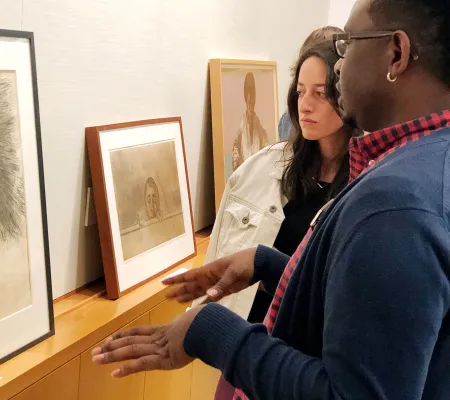 two people looking at and discussing framed prints on shelf 