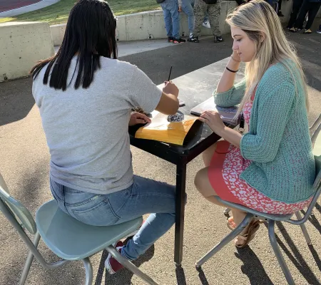 picture of a white woman teaching a student outside on a table