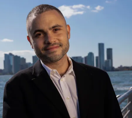 Thomas J Lax Curator of Media and Performance at MoMA and invited guest for the University of Texas at Austin's esteemed Viewpoint Lecture Series smiling in front of a body of water