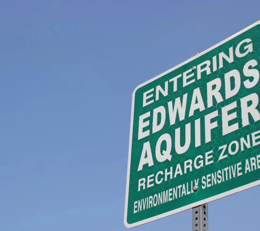 green sign with text that reads Entering Edwards Aquifer Recharge against blue sky Zone