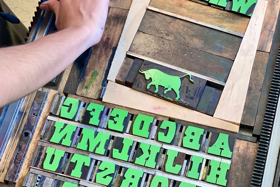 person locking up wooden type on bed of printing press